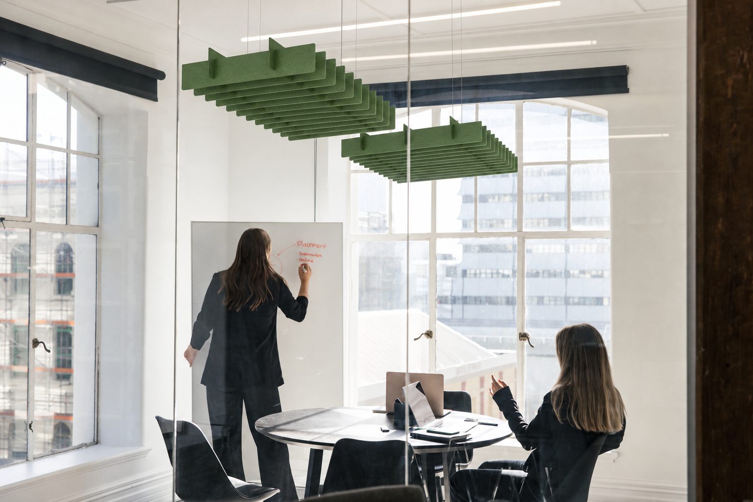 A meeting room with two green slatted acoustic baffles hanging over the table