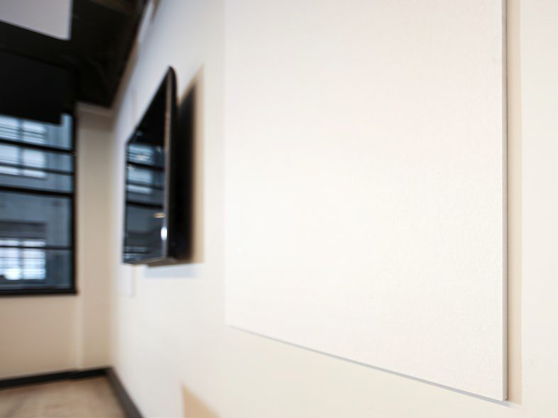 A plain white whiteboard fixed to a meeting room wall, beside a wall-mounted screen