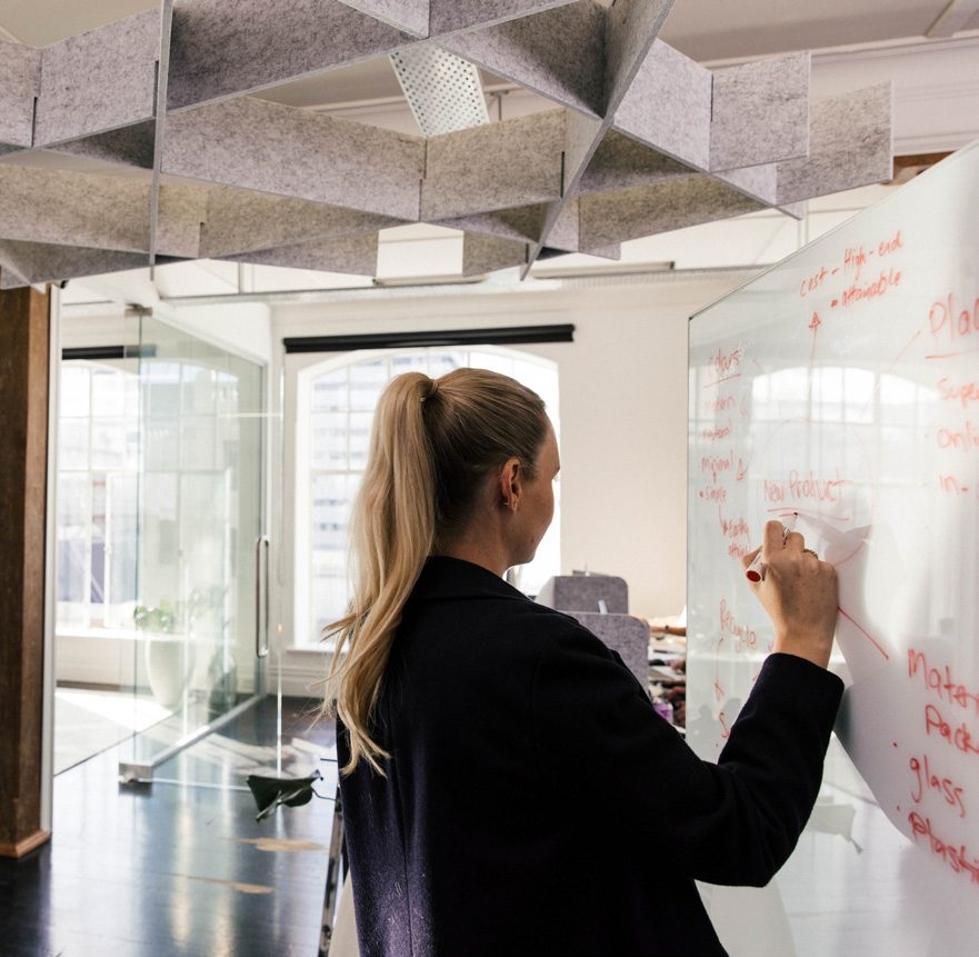 A woman writing on a glassboard in a meeting room under acoustic ceiling panels